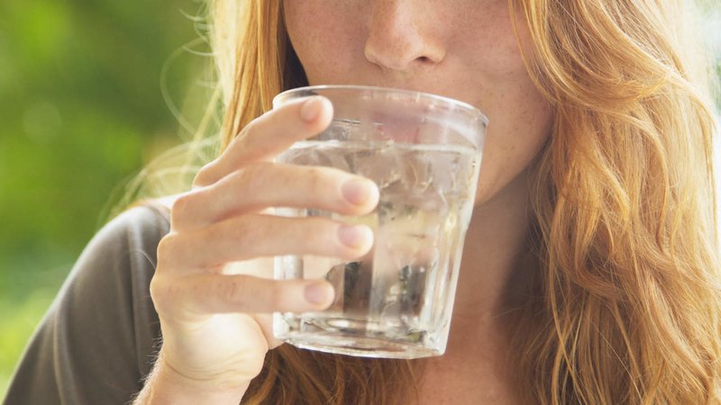 A Woman Taking A Drink Of Water From A Glass